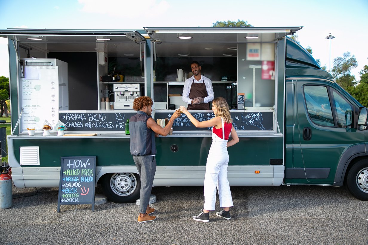 Diverse couple clinking beer at counter of food trailer